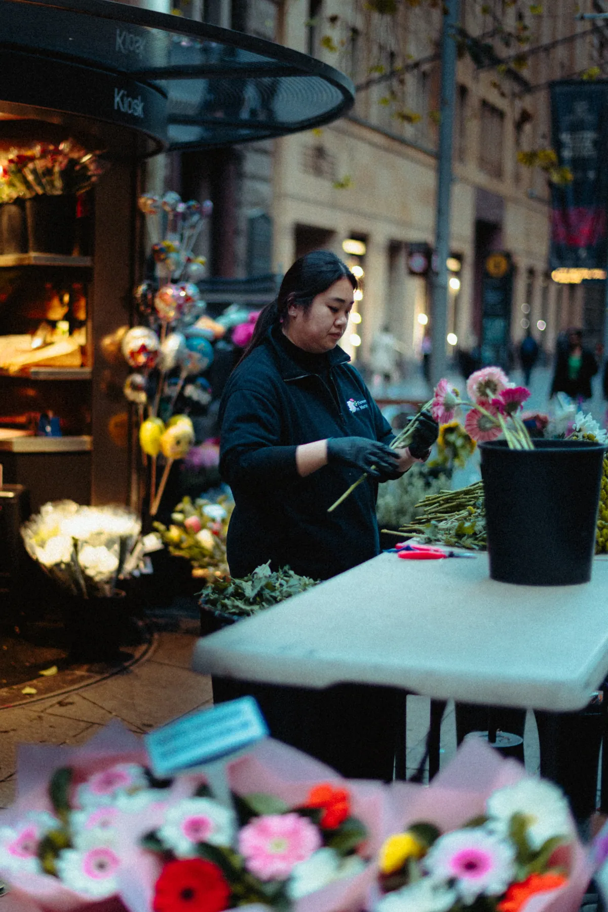 A florist arranging gerberas at her stall beneath warm shop lights
