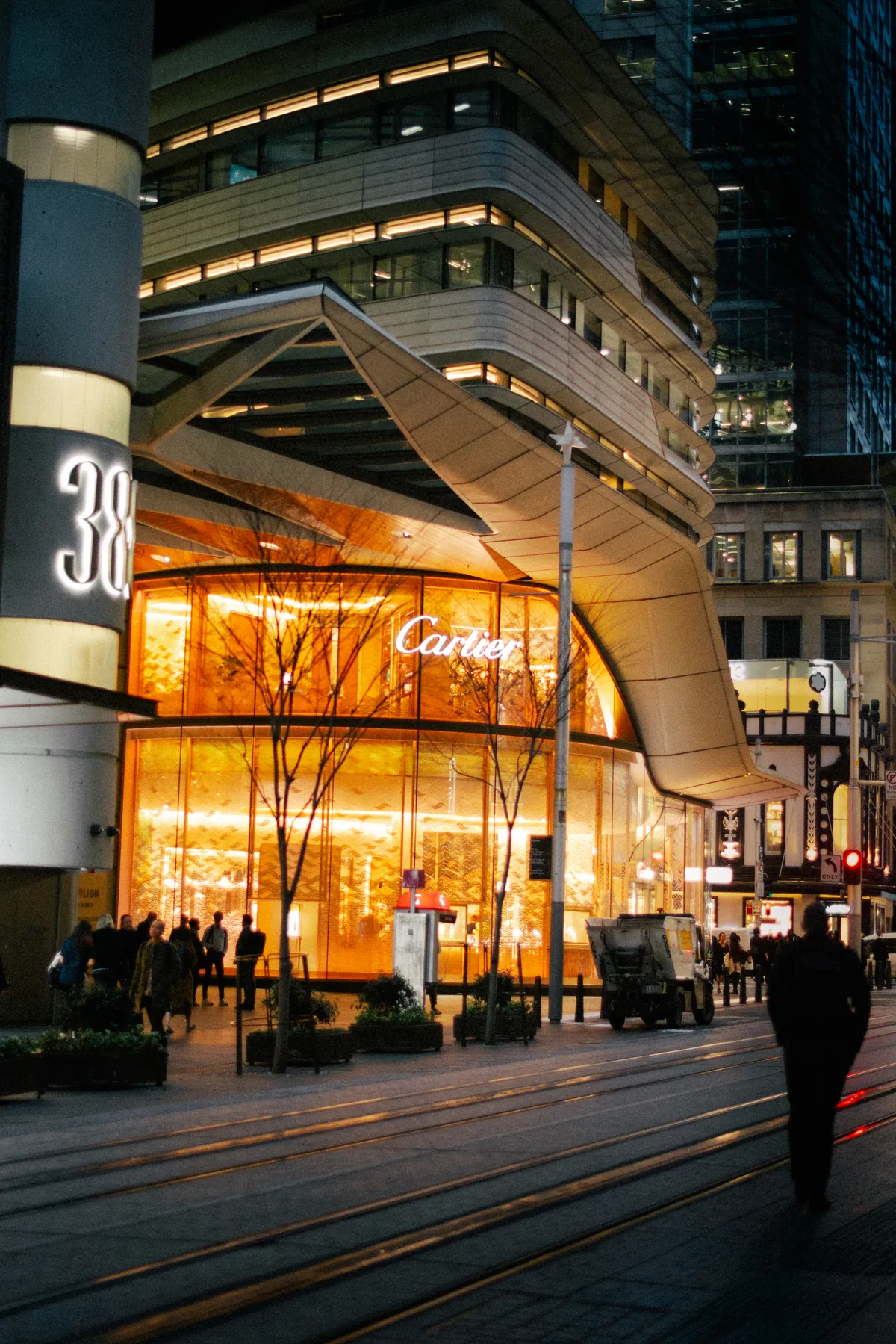 A curved glass tower with a glowing jewellery store at street level at dusk