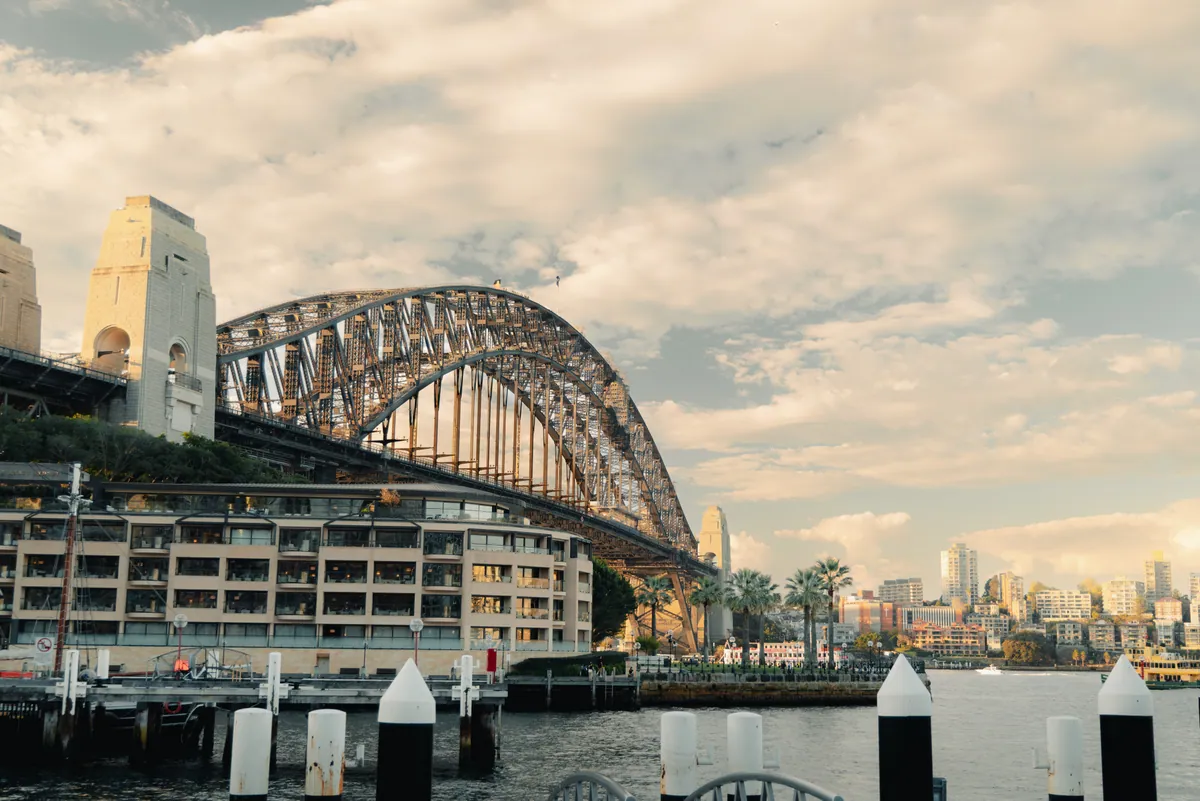 The Harbour Bridge arching over harbourside buildings and wharf piles